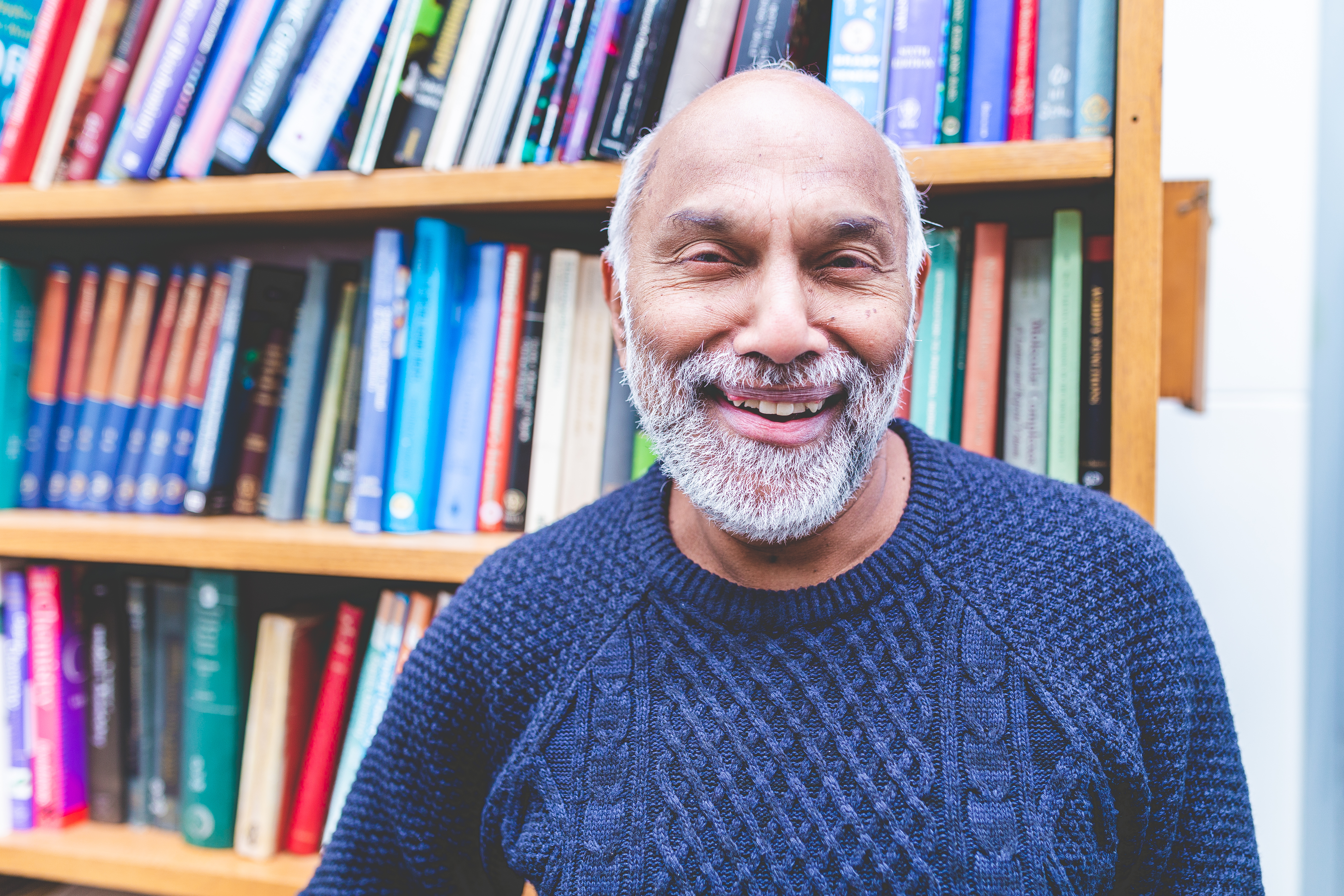 AP de Silva smiling in front of large bookcase